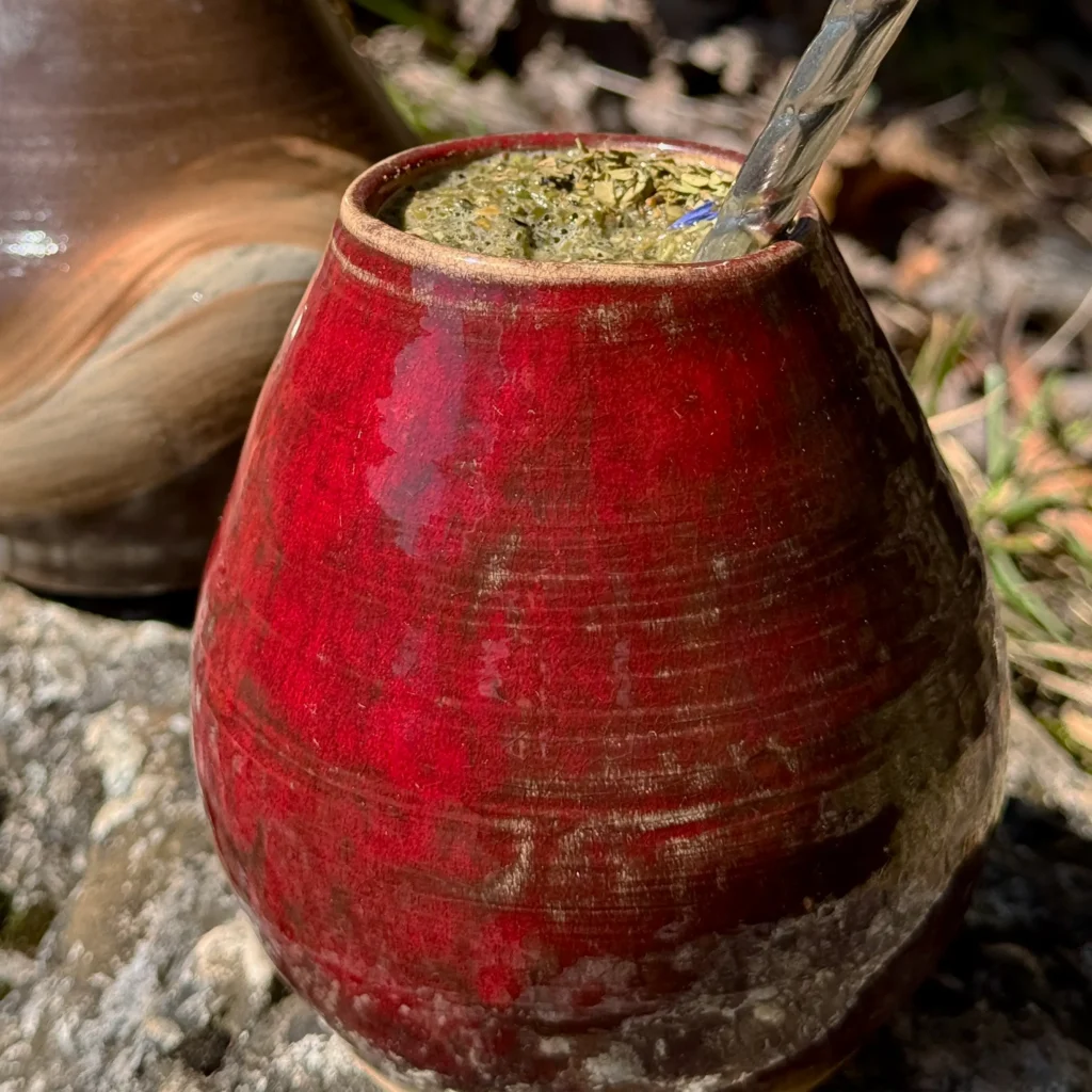 Červená keramická kalabasa Velvet plná yerba maté s bombillou položená na kameni v prírode.