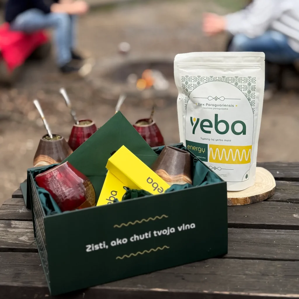 Otvorený yeba DuoBox na drevenom stole pri ohnisku v prírode s balením yeba energy 400 g a štyrmi kalabasami s bombillami.